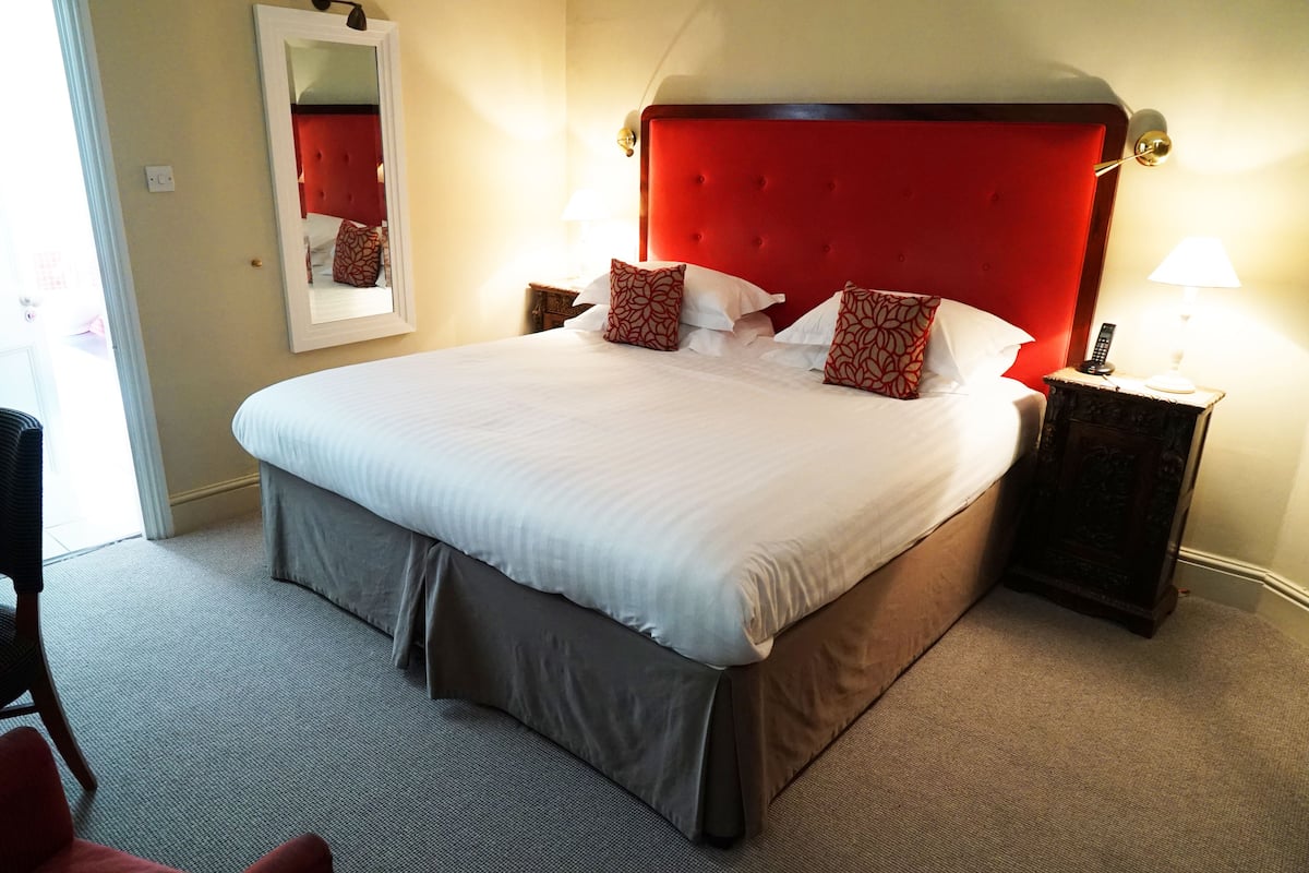 A large bed with a red headboard, two bedside tables with lamps, and a mirror on the wall.