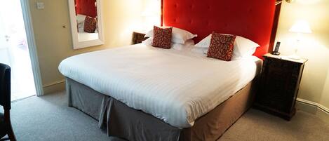 Una cama grande con cabecera roja, dos mesitas de noche con lámparas y un espejo en la pared.