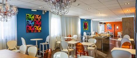 A modern dining area with white and orange chairs, a wooden table, and a chandelier.