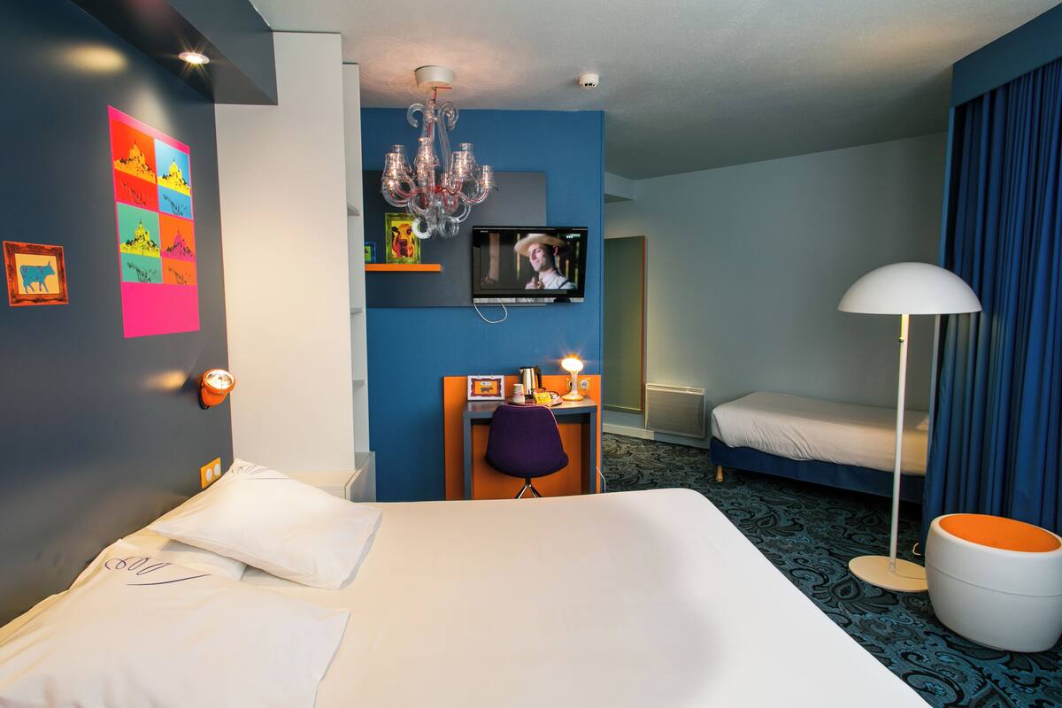 Ein Hotelzimmer mit einem großen Bett, einem Schreibtisch mit Stuhl, einem Fernseher, einer Chandelier und einem Badezimmer mit Toilette und Waschbecken.