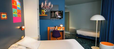 A hotel room with a large bed, a desk with a chair, a television, a chandelier, and a bathroom with a toilet and sink.