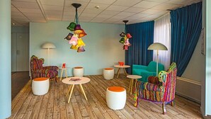 A room with wooden flooring, colorful chairs, round tables, and a blue sofa. - Hôtel Gabriel (Le Mont-Saint-Michel)