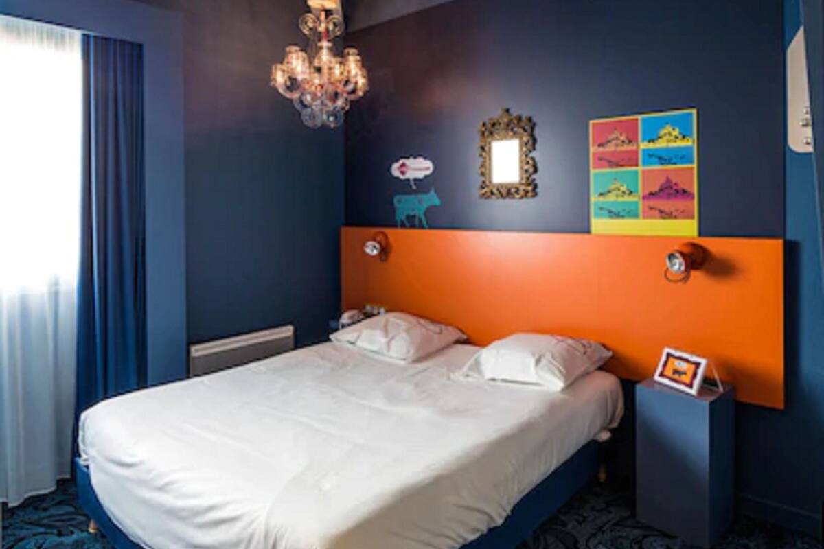 Ein Schlafzimmer mit einem Bett, einer Kristalllüster, einem Spiegel und einem farbenfrohen Kunstwerk an der Wand.