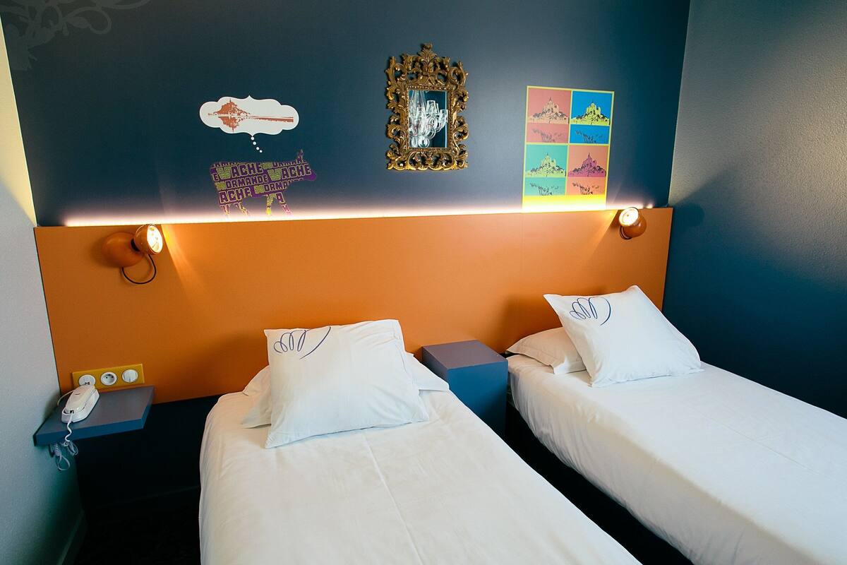 Ein Hotelzimmer mit zwei Betten, einem Nachttisch mit Telefon, einer Wandleuchte und Dekoration.
