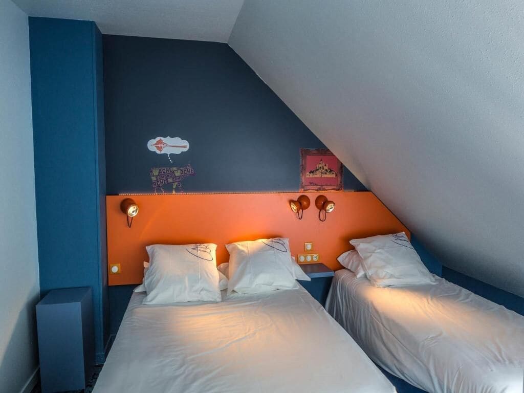 Una habitación con dos camas, una pared de acento azul, un reloj y luces fijadas a la pared.