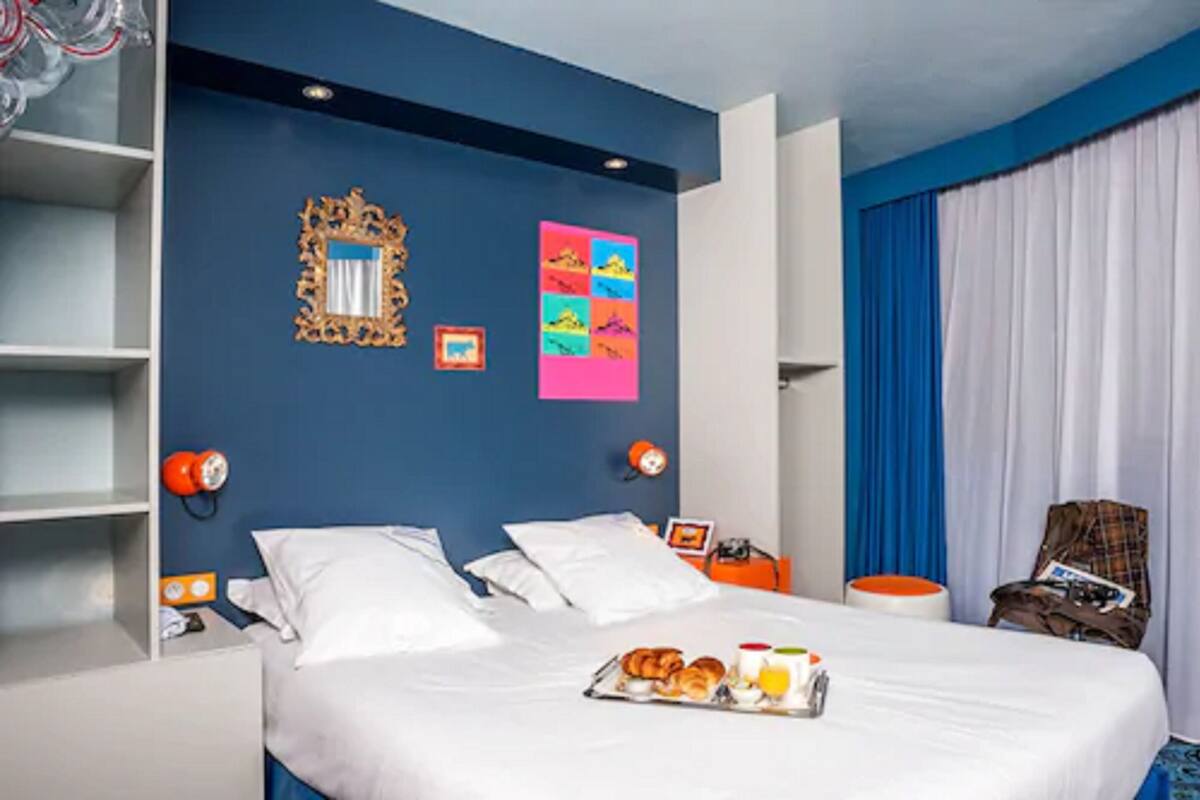 Ein Hotelzimmer mit Bett, Frühstücksbrett, Spiegel und einem farbenfrohen Kunstwerk an der Wand.