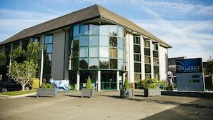 A modern hotel with a curved glass facade, a signboard, and a parking area. - Hôtel Gabriel (Le Mont-Saint-Michel)