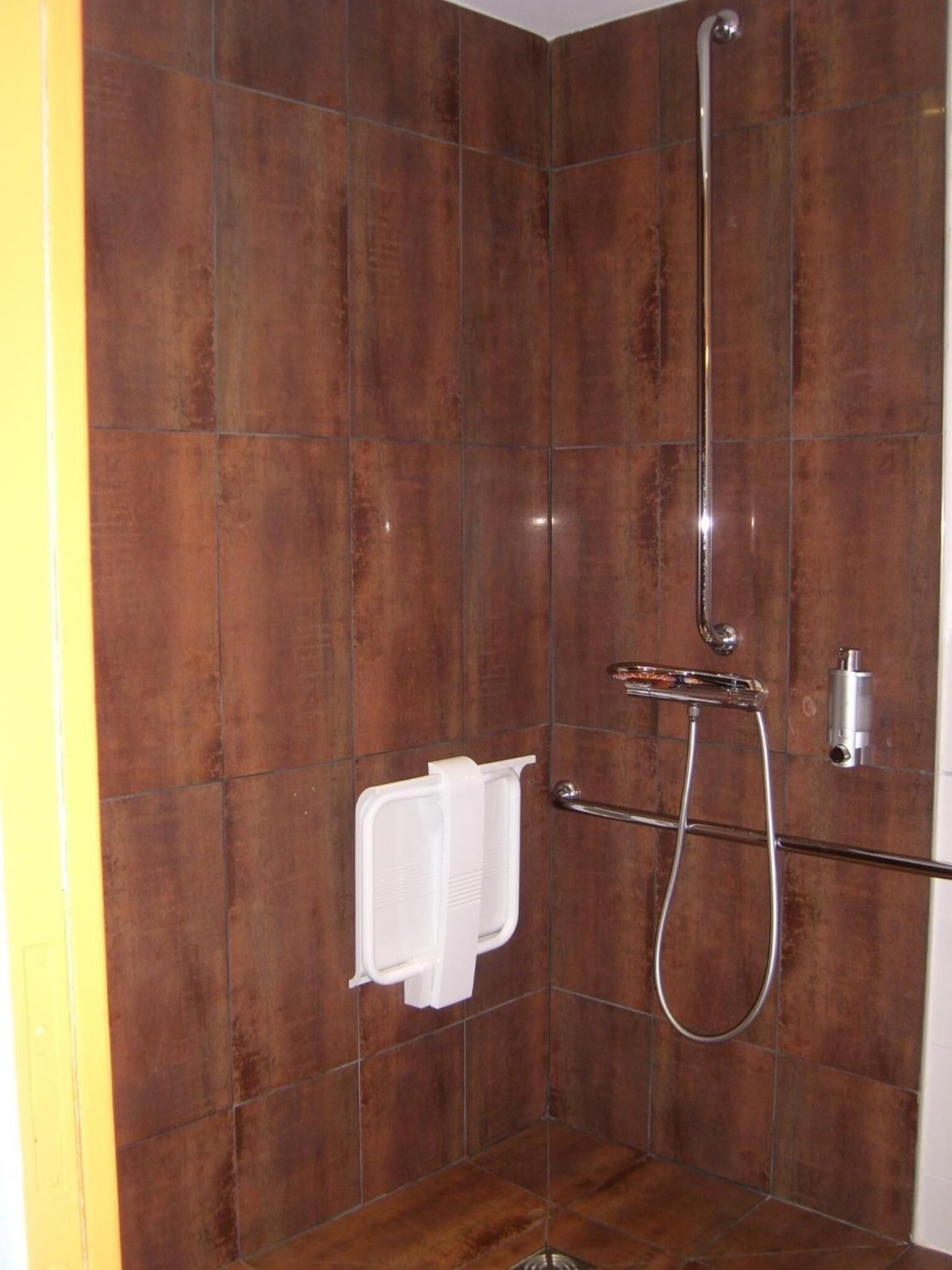 Un espace douche avec des carreaux marron, un porte-serviettes blanc et une pomme de douche chromée.