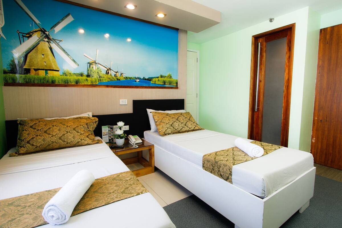 A hotel room with two beds, a mural of windmills, a wooden door, and a nightstand with a phone.