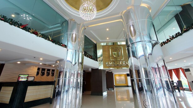 A modern hotel lobby with a reception desk, a chandelier, and a large glass column.