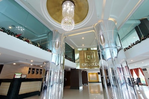 Un moderno vestíbulo de hotel con un mostrador de recepción, una araña de cristal y una gran columna de vidrio.