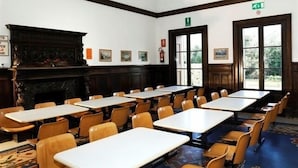 Een vergaderruimte met houten tafels en stoelen, een open haard en ingelijste foto’s aan de wanden.
