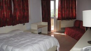 Un dormitorio con una cama, un escritorio con lámpara, una silla y una ventana con cortinas.
