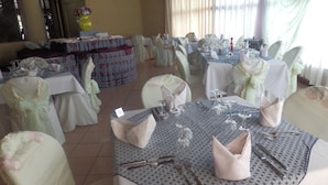 Un salón de banquetes con mesas redondas dispuestas para un evento formal, que incluye manteles, sillas y cubiertos.