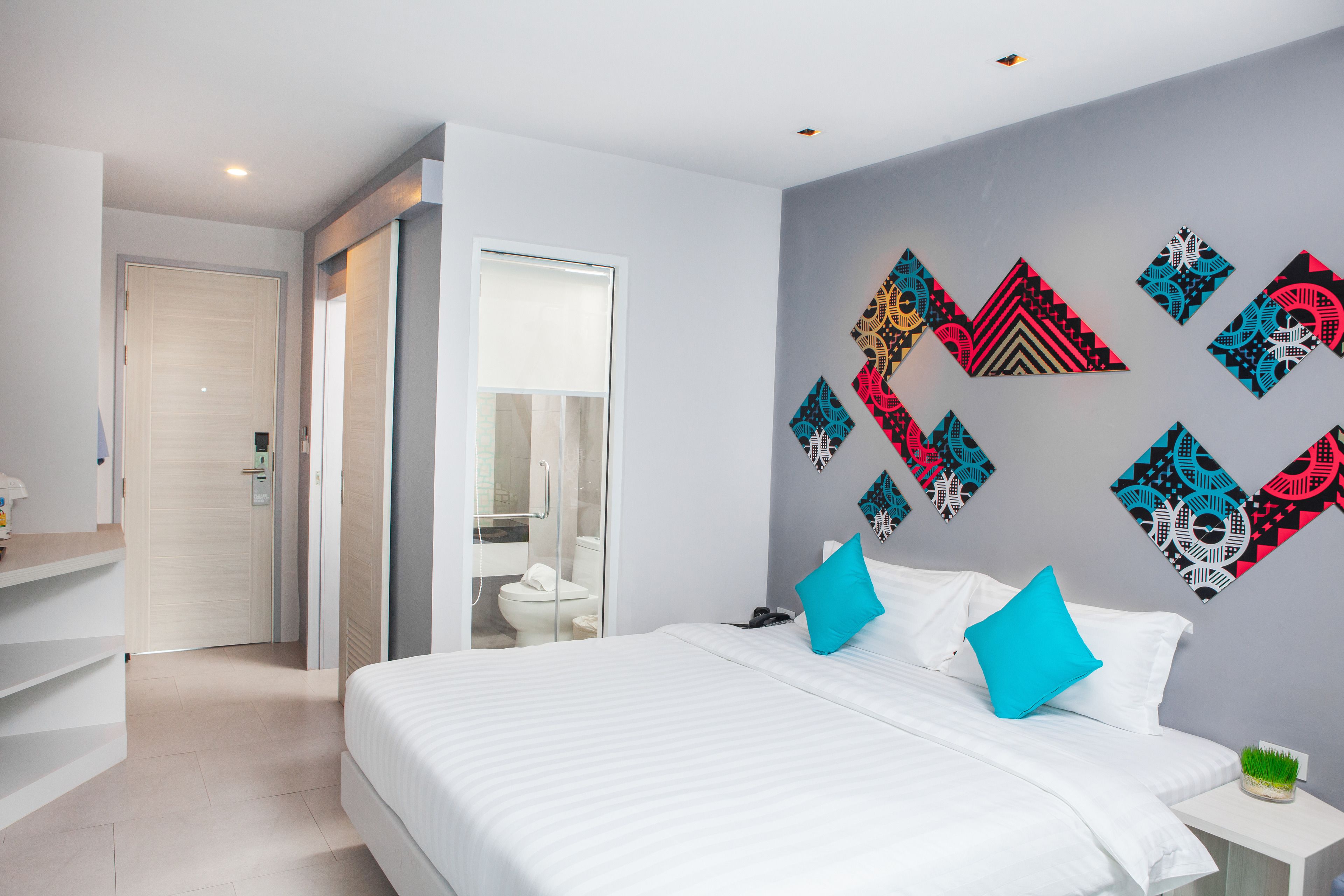 Una habitación de hotel moderna con una cama grande, una mesita de noche y un baño visible a través de una puerta abierta.