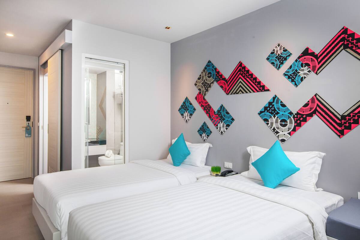 A hotel room with two beds, a bathroom, and a wall decorated with geometric patterns.