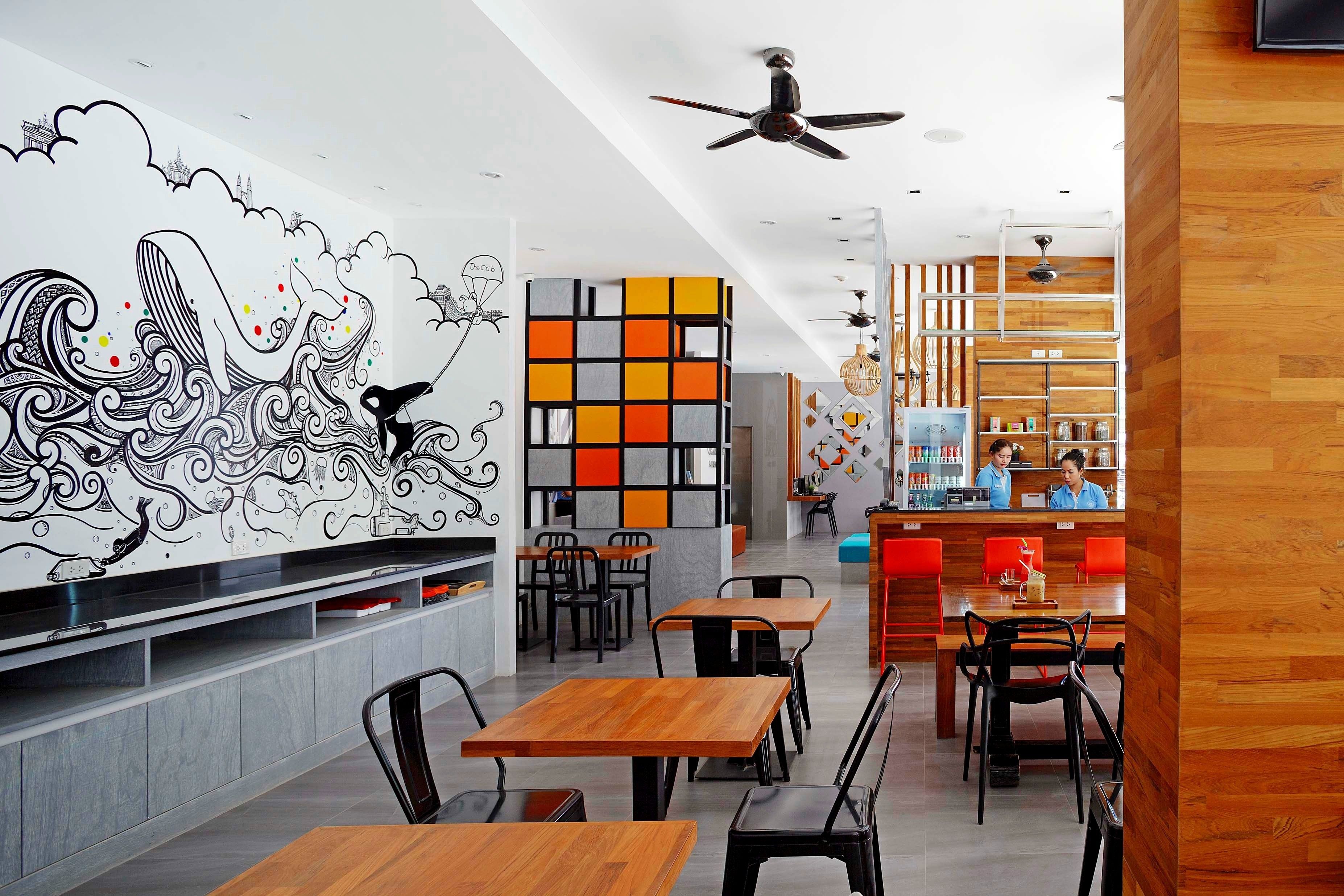 A modern cafe with wooden tables and chairs, a colorful wall art, and a bar area with staff.
