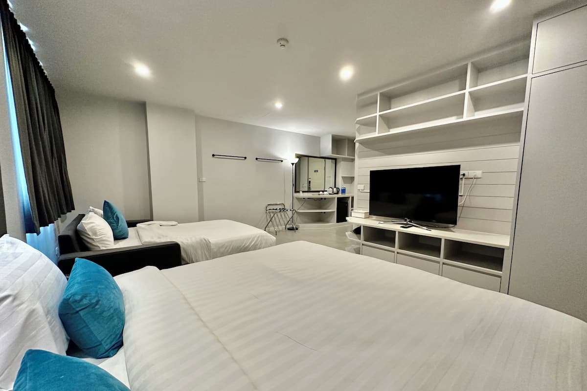 A modern hotel room with two beds, a large flat-screen TV, a vanity with a mirror, and built-in shelving.