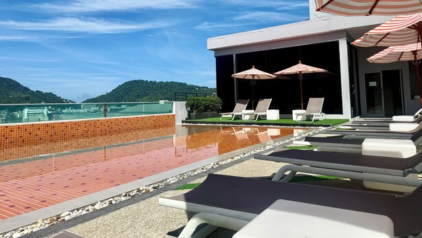 Un espace piscine aménagé sur le toit, avec des chaises longues et des parasols à rayures, offrant une vue sur un paysage montagneux.