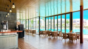A spacious indoor area with a pool view, wooden flooring, and wicker furniture. - Hotel Floresta (Tías)