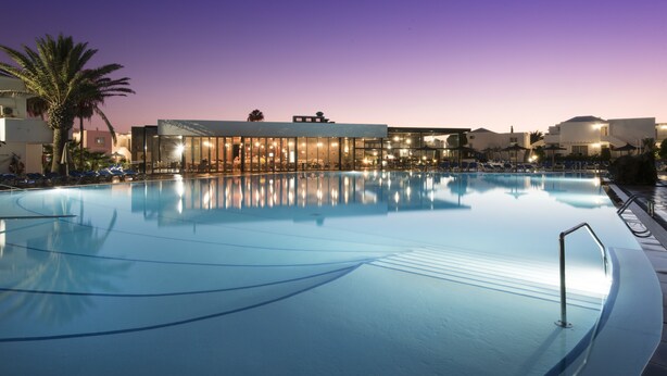 A swimming pool with a modern building in the background. - Hotel Floresta (Tías)