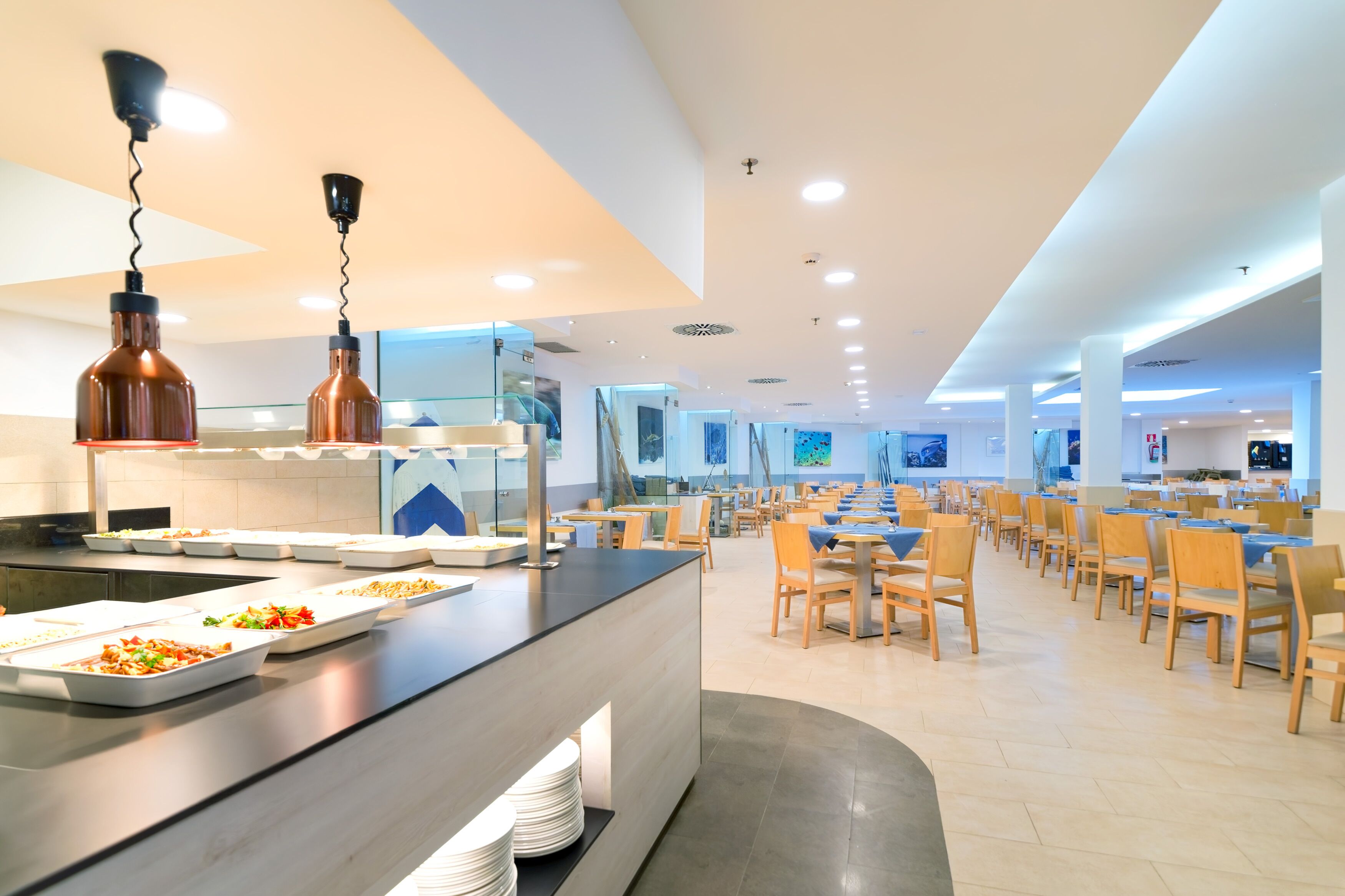 A modern dining area with a long counter, multiple seating arrangements, and pendant lighting.