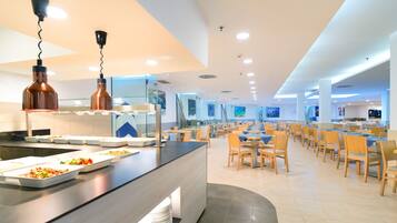 A modern dining area with a long counter, multiple seating arrangements, and pendant lighting.