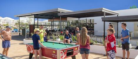 An outdoor pool area with a pool table, seating, and a covered pavilion.