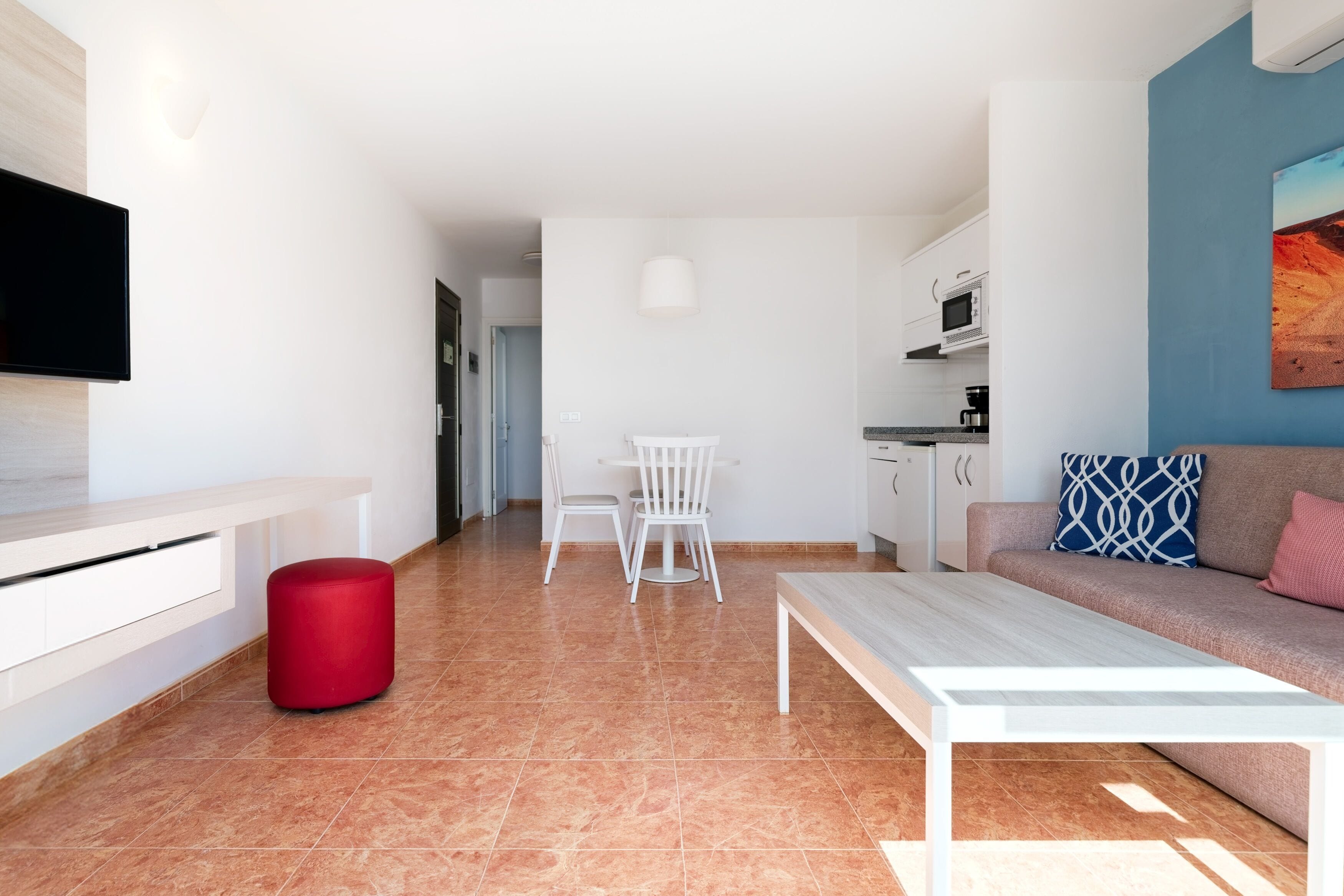 Una sala de estar moderna con sofá, una mesa de centro, televisor, comedor con sillas y una cocina al fondo.