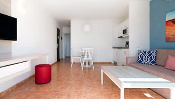 Una sala de estar moderna con sofá, una mesa de centro, televisor, comedor con sillas y una cocina al fondo.