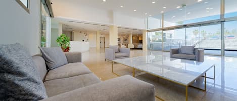 Un vestíbulo moderno con un sofá, sillones, una mesa de centro de mármol y grandes ventanales con vistas.