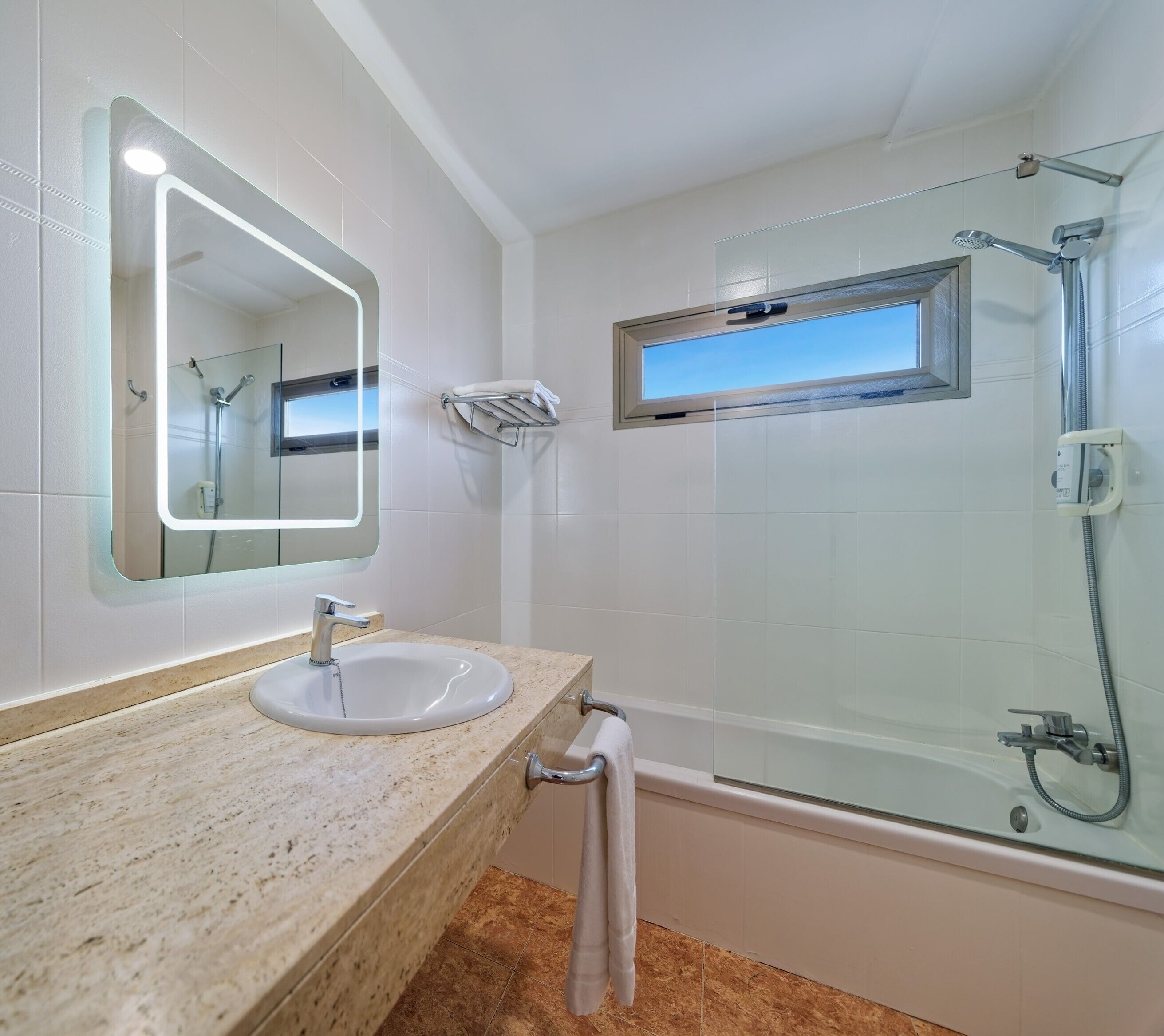 Ein Badezimmer mit Waschbecken, Spiegel, Handtuchhalter, Dusche und einem Fenster.