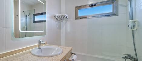 Ein Badezimmer mit Waschbecken, Spiegel, Handtuchhalter, Dusche und einem Fenster.