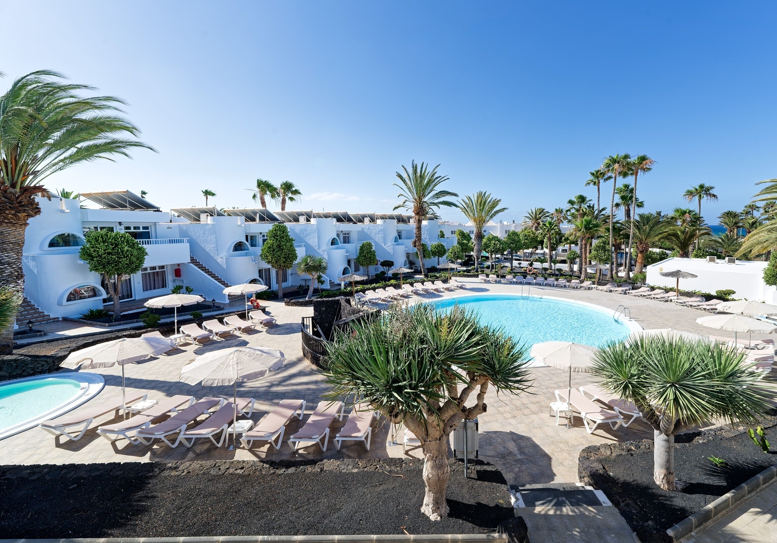 A resort with multiple swimming pools, lounge areas, palm trees, and white buildings.