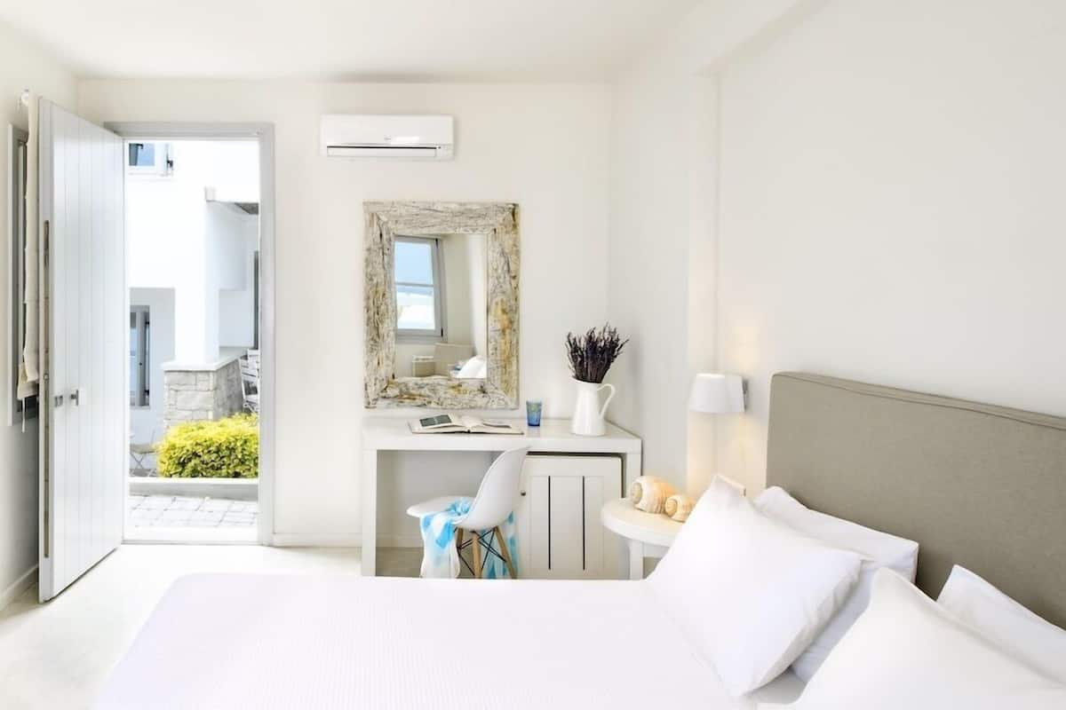 A hotel room with a bed, a desk, a chair, a mirror, and a view of the outside.