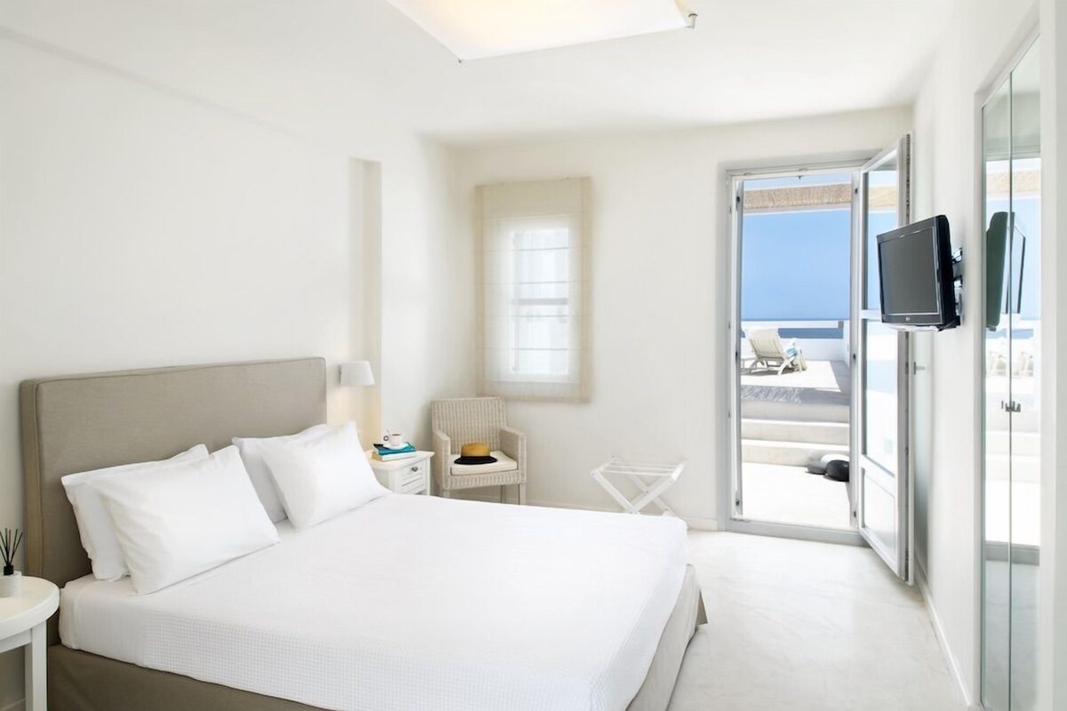 Habitación de hotel con cama, una silla, televisor y balcón con vistas.