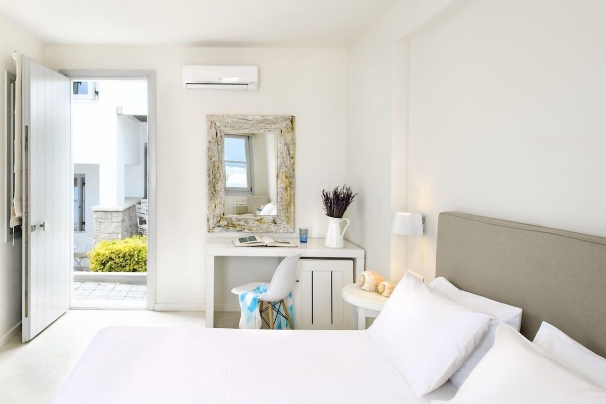 Ein Hotelzimmer mit Bett, Schreibtisch, Stuhl, Spiegel und Blick ins Freie.