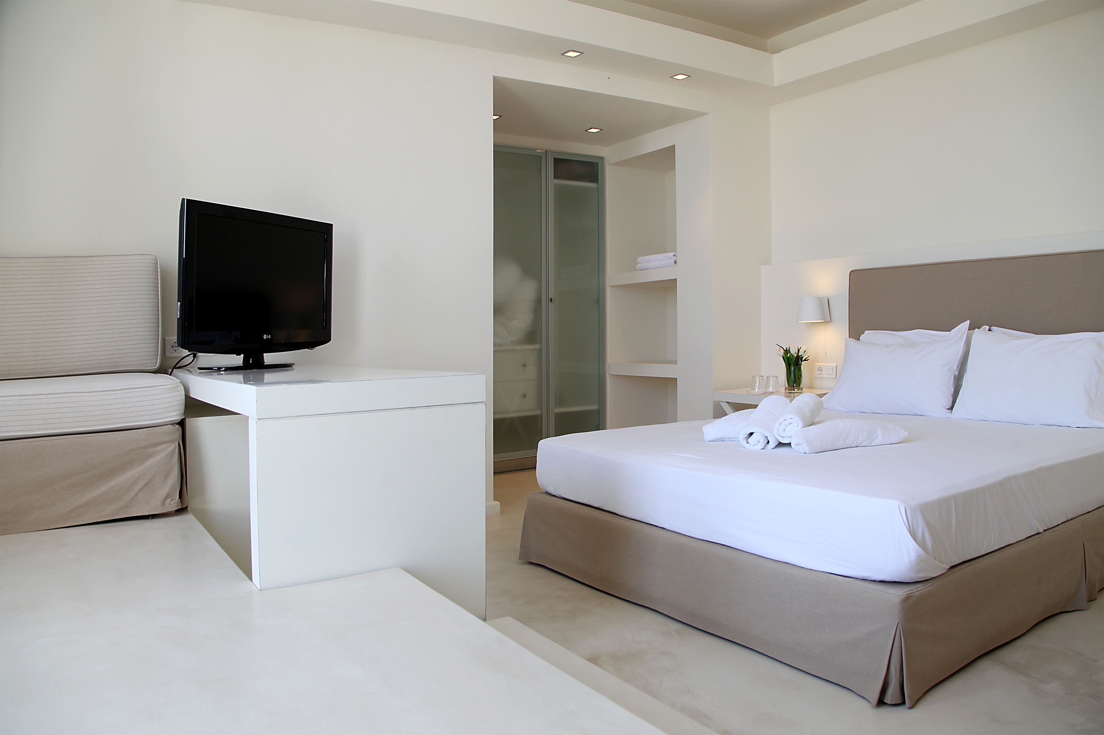 Ein modernes Hotelzimmer mit Bett, Fernseher, Schreibtisch und begehbarem Kleiderschrank.