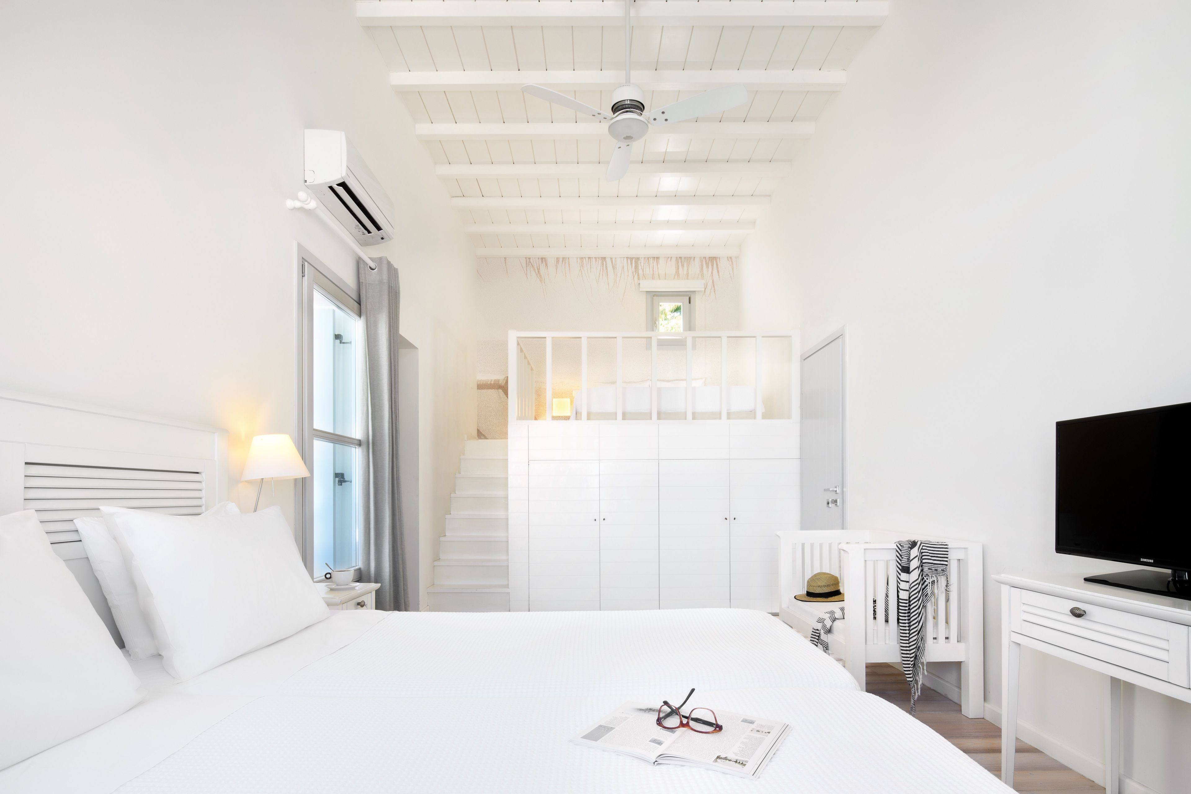 Ein modernes Hotelzimmer mit einem Bett, einem Fernseher, einem Schreibtisch und einer Treppe zu einer oberen Ebene.