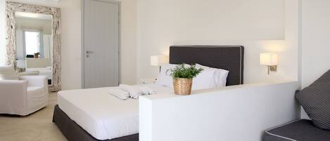 A modern hotel room with a large bed, a bedside table with a lamp, a chair, and a small table with a plant.