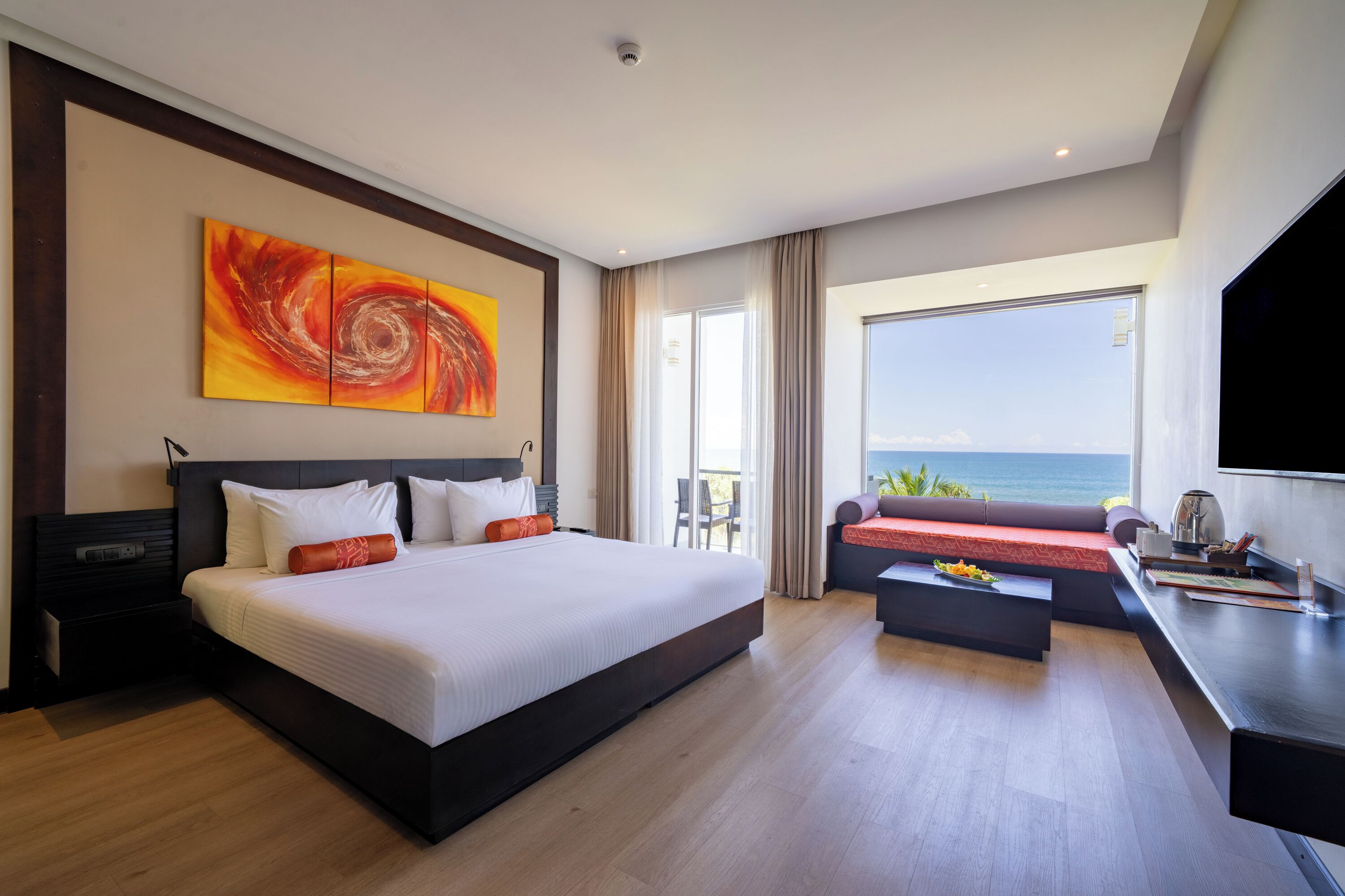 A hotel room with a large bed, a sofa, a desk, and a view of the sea.