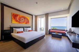 Habitación de hotel con una cama grande, un sofá, un escritorio y vistas al mar.