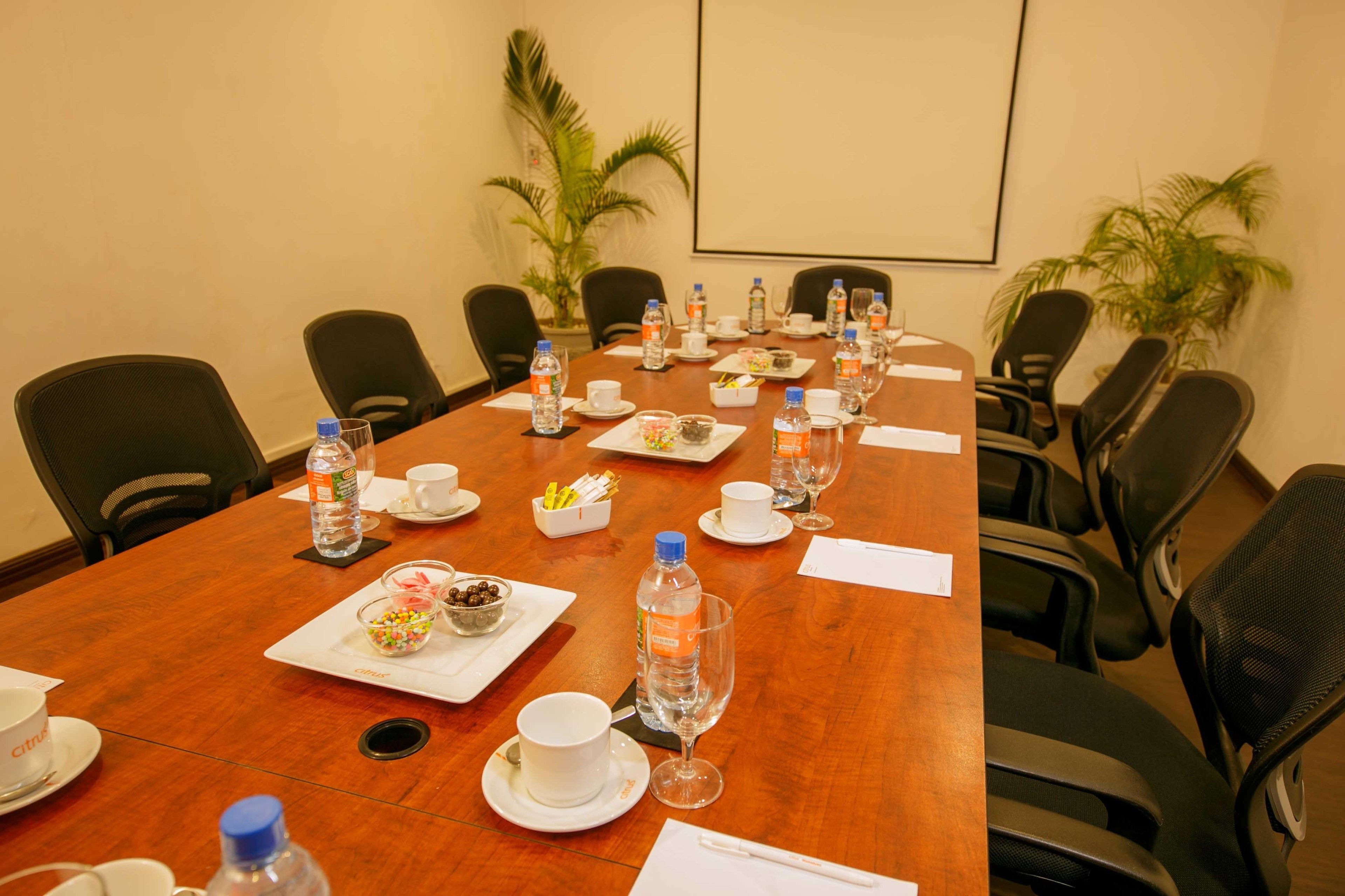 A conference room with a long table set for a meeting, equipped with water bottles, cups, and a small bowl of snacks.