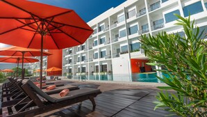 A poolside area with sun loungers and red umbrellas, a modern building with balconies, and a clear blue sky. - Citrus Waskaduwa (Wadduwa)