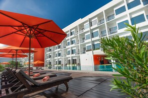 A poolside area with sun loungers and red umbrellas, a modern building with balconies, and a clear blue sky. - Citrus Waskaduwa (Wadduwa)