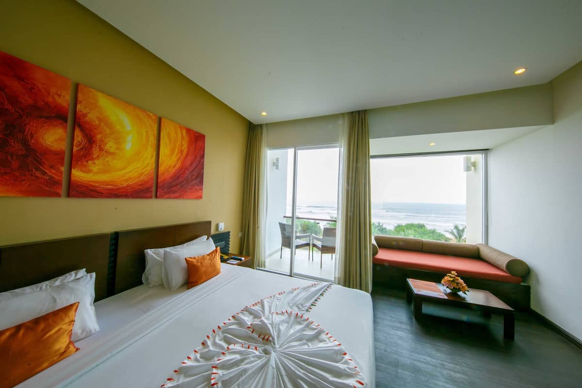 A hotel room with a large bed, a sofa, a coffee table, and a view of the ocean.