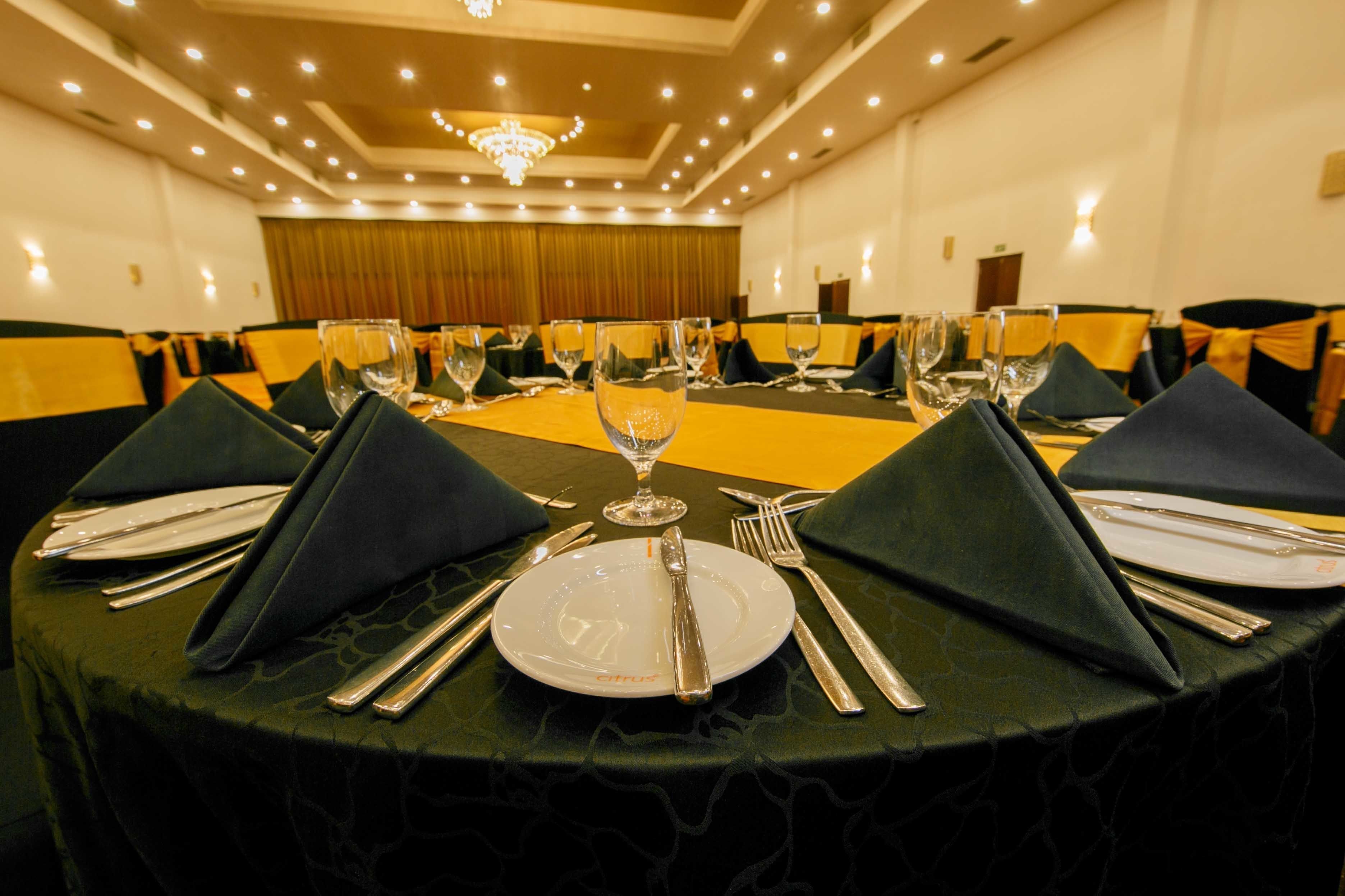 A banquet hall with round tables set for dining, each with a white plate, silverware, and a wine glass.