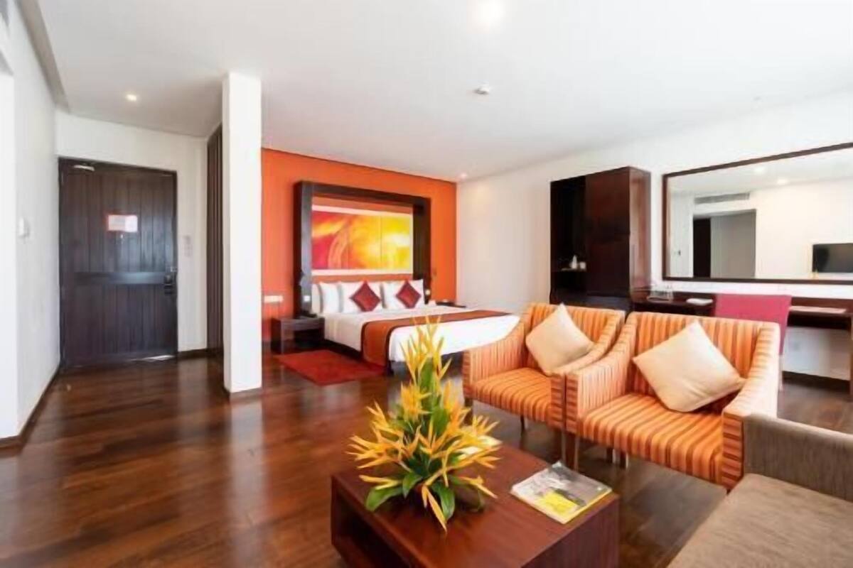 A hotel room with a bed, a sofa, a coffee table with a plant, and a large mirror.