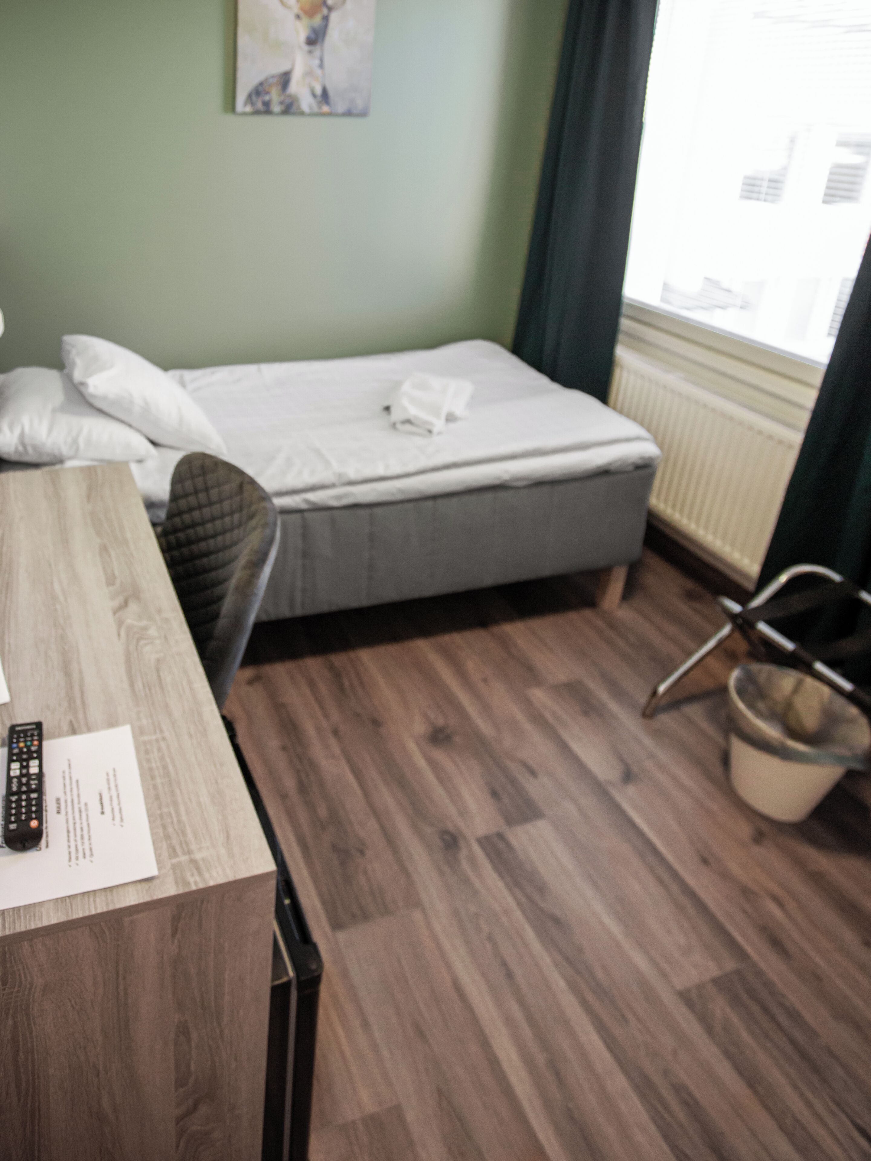 A room with a bed, a wooden desk, a chair, a radiator, and a window with curtains.