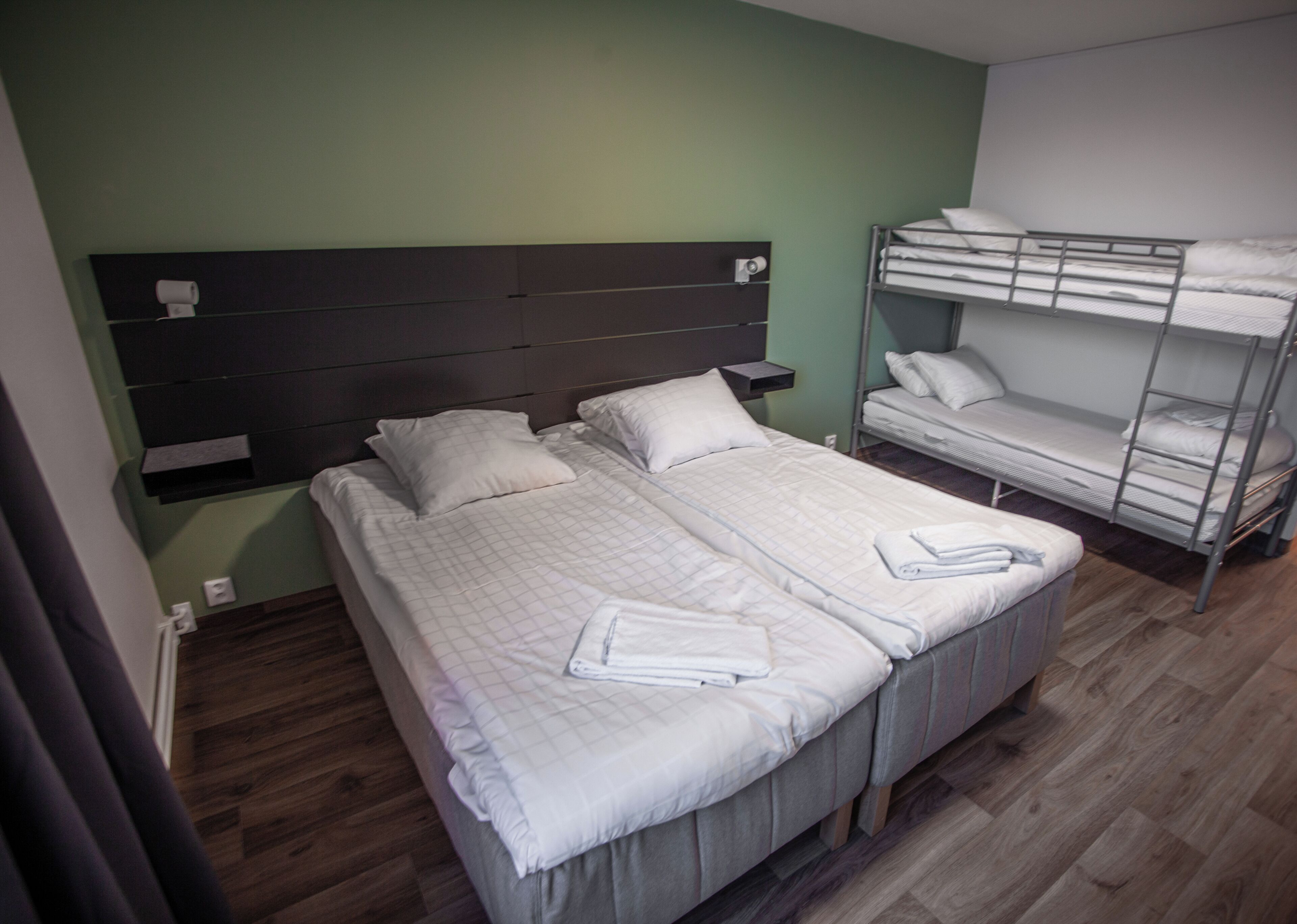 A room with a bed, a bunk bed, a headboard, a bedside table, and a wall-mounted shelf.